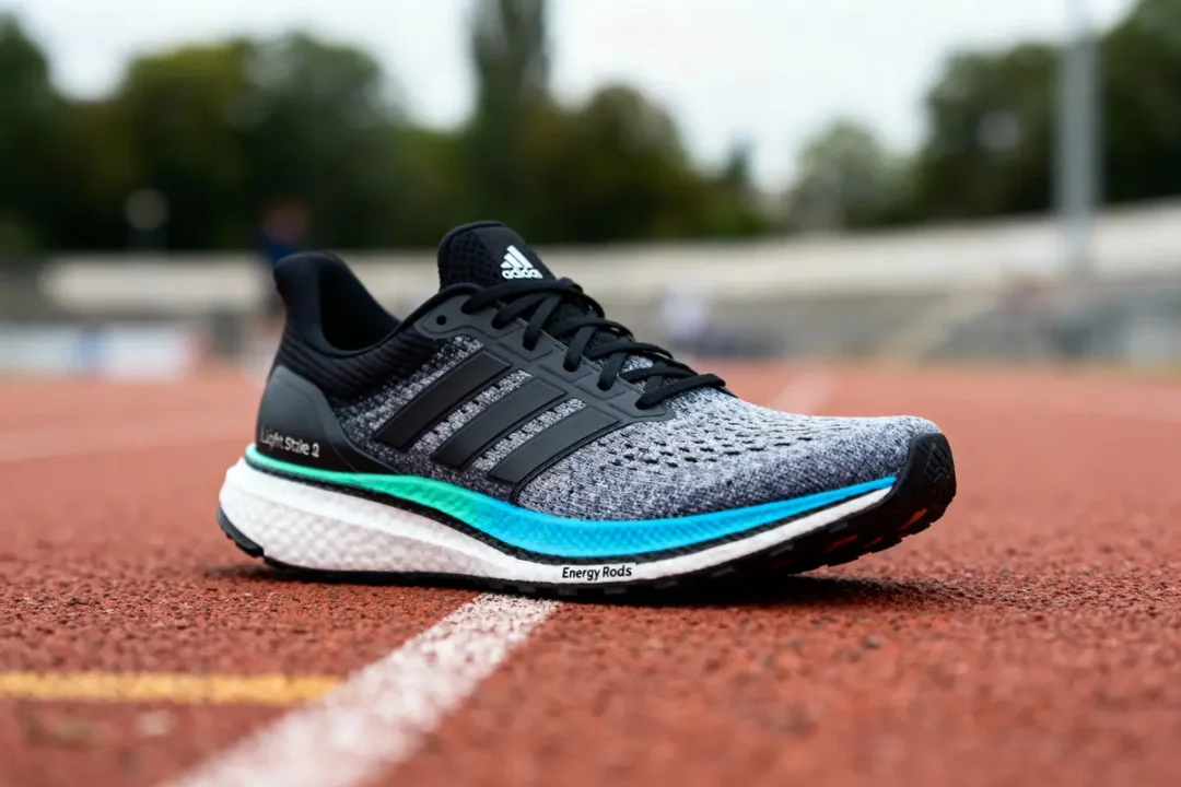 Chaussure de course Adidas grise, noire et turquoise sur une piste d'athlétisme rouge.