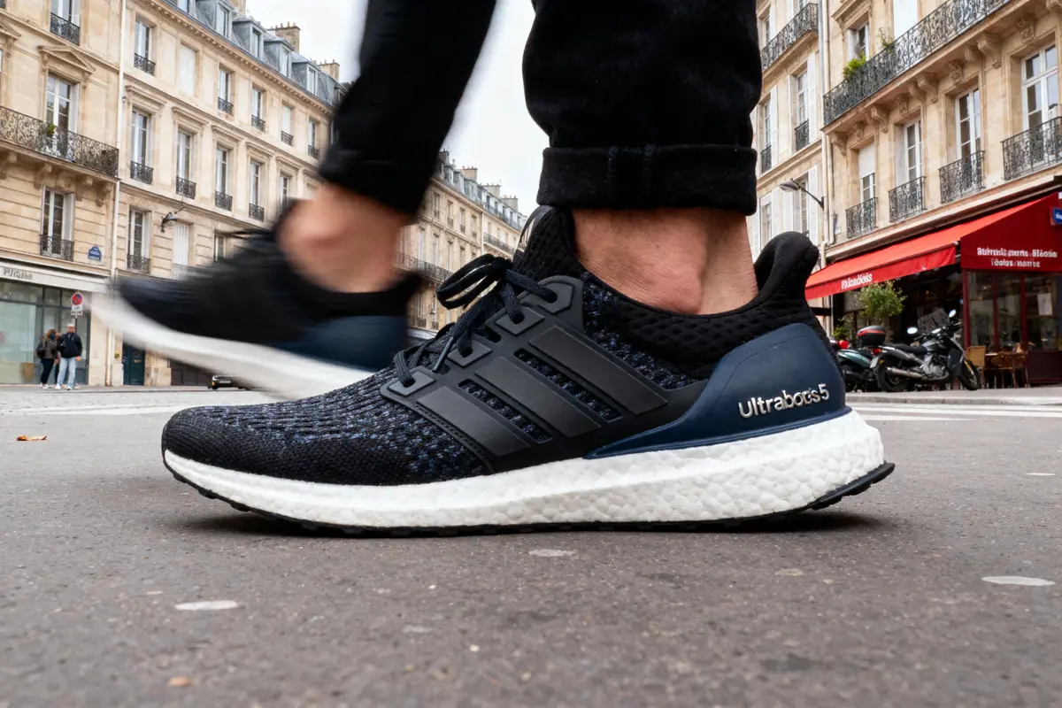 Gros plan sur des baskets noires "Ultraboots" dans une rue parisienne, passants en arrière-plan.