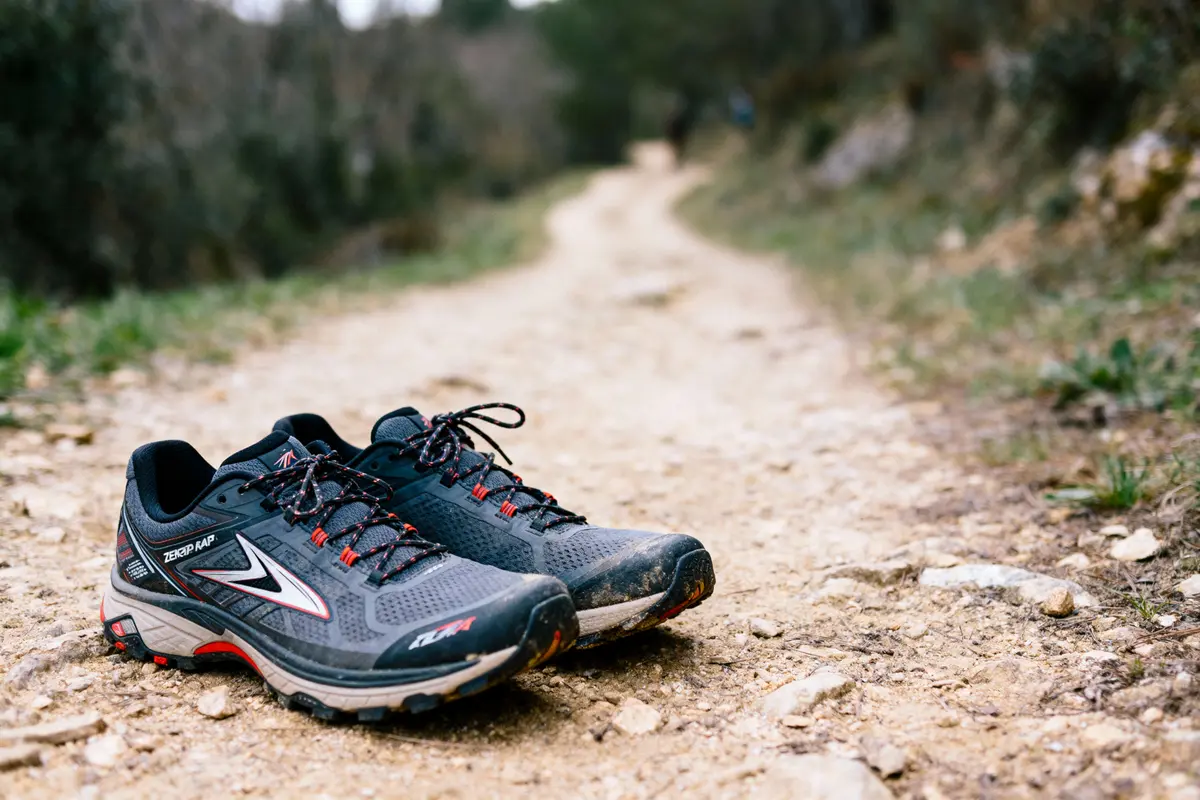 Chaussures de course noires sur un chemin de terre en plein air, entourées de verdure floue.