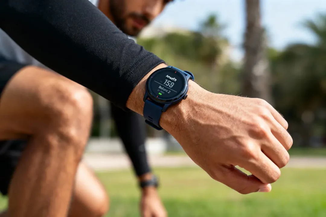 Homme portant montre connectée bleue, montre affichant fréquence cardiaque, contexte extérieur.