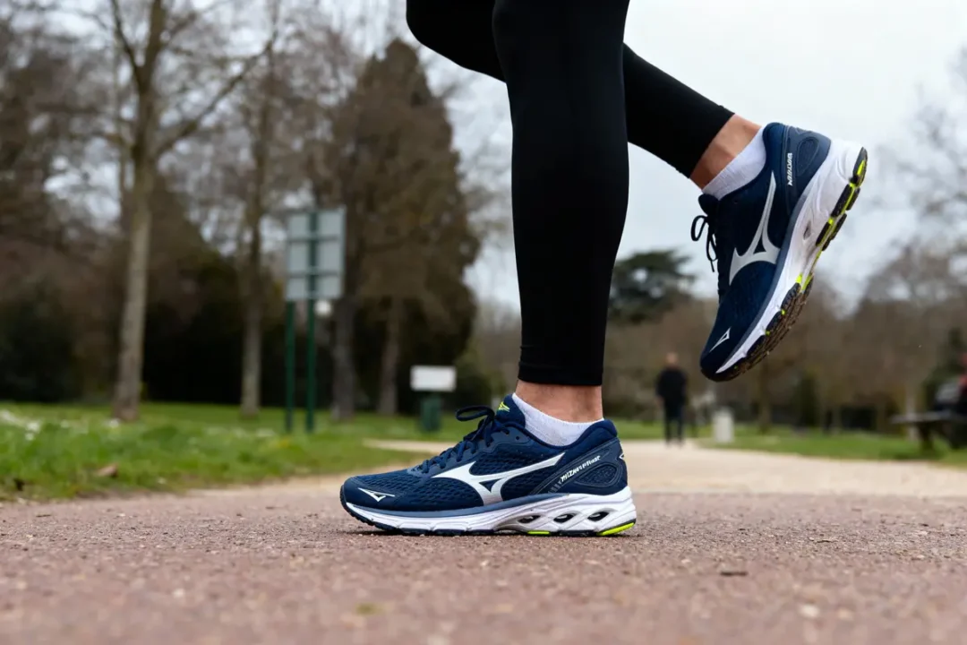 Personne courant sur un chemin, portant des chaussures de course bleues et noires, parc arboré en arrière-plan.