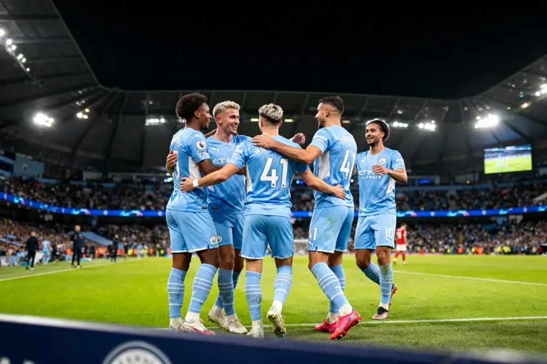 Joueurs de football célébrant un but sur le terrain, foule en arrière-plan dans un stade illuminé.