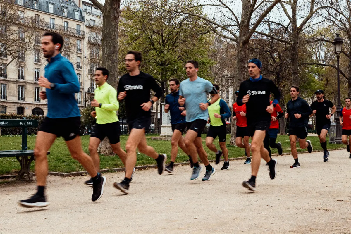 Groupe de personnes courant dans un parc urbain avec des arbres et des bâtiments en arrière-plan.