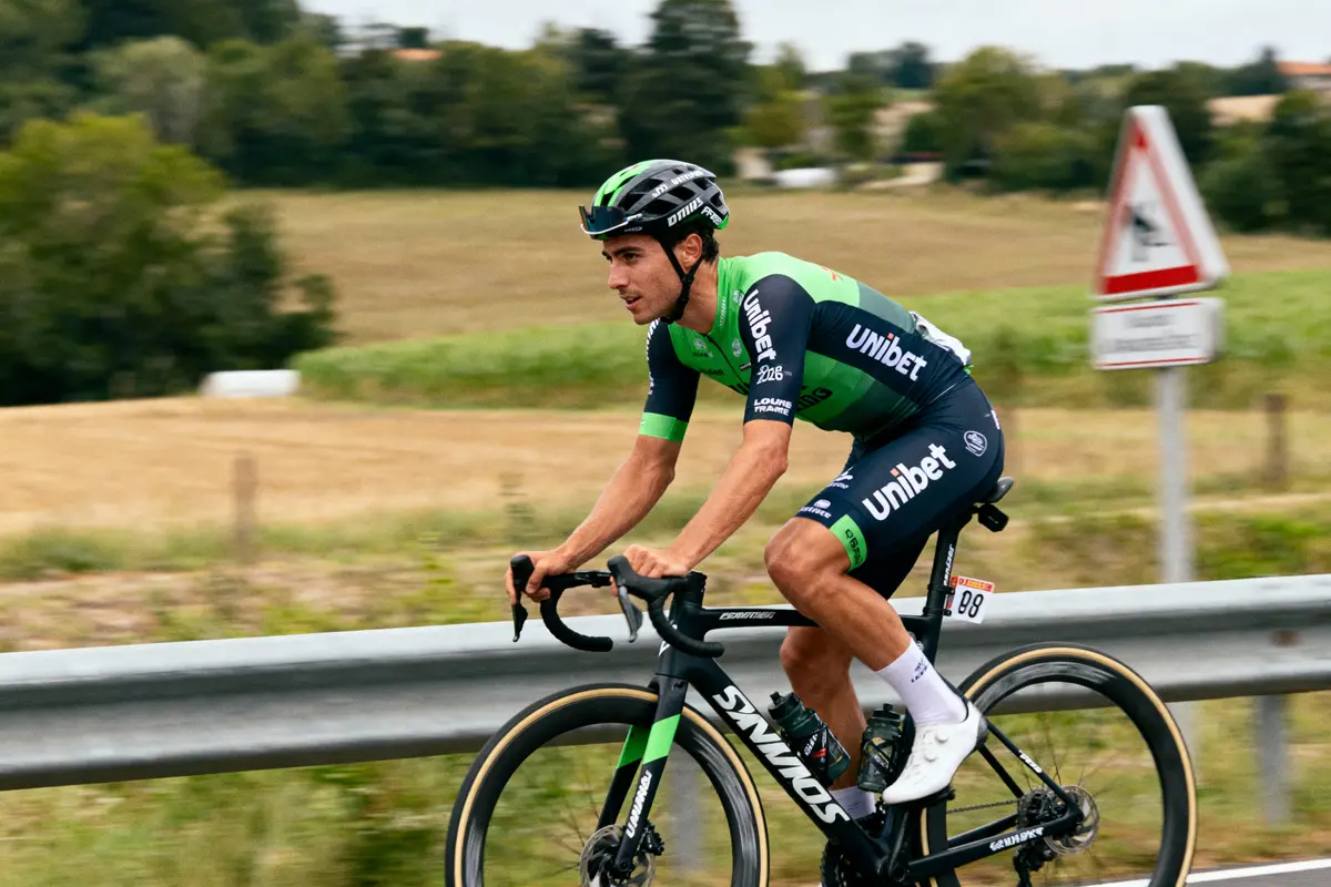 Cycliste portant maillot vert et noir Unibet, roulant sur route de campagne, sur vélo route Specialized.