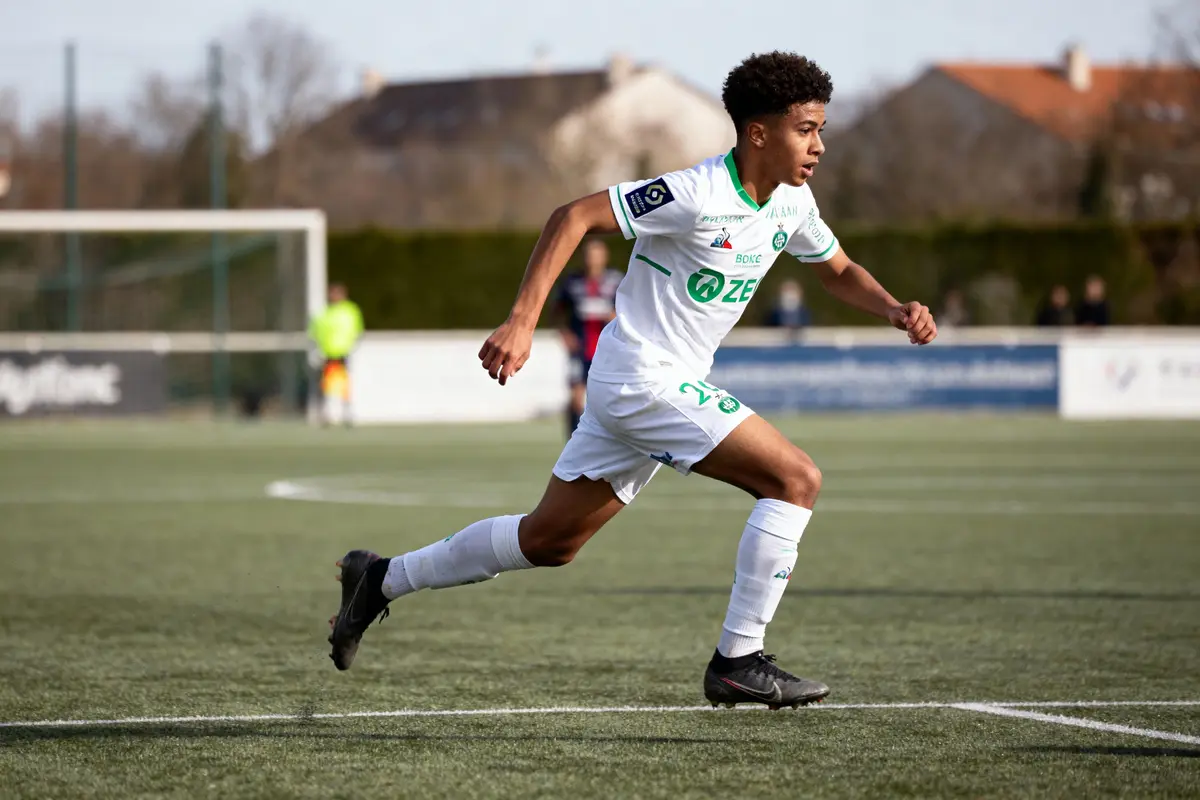 Joueur de football en action sur un terrain, portant un maillot blanc avec sponsor visible.