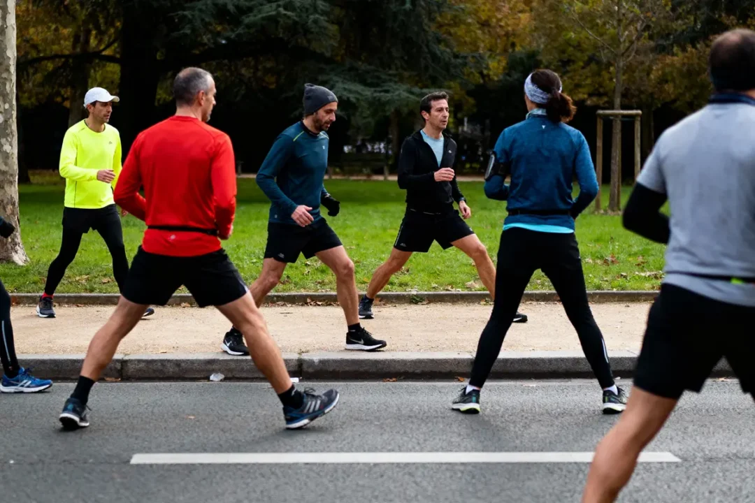 Groupe de personnes faisant des exercices de course dans un parc, entouré de verdure et d'arbres.