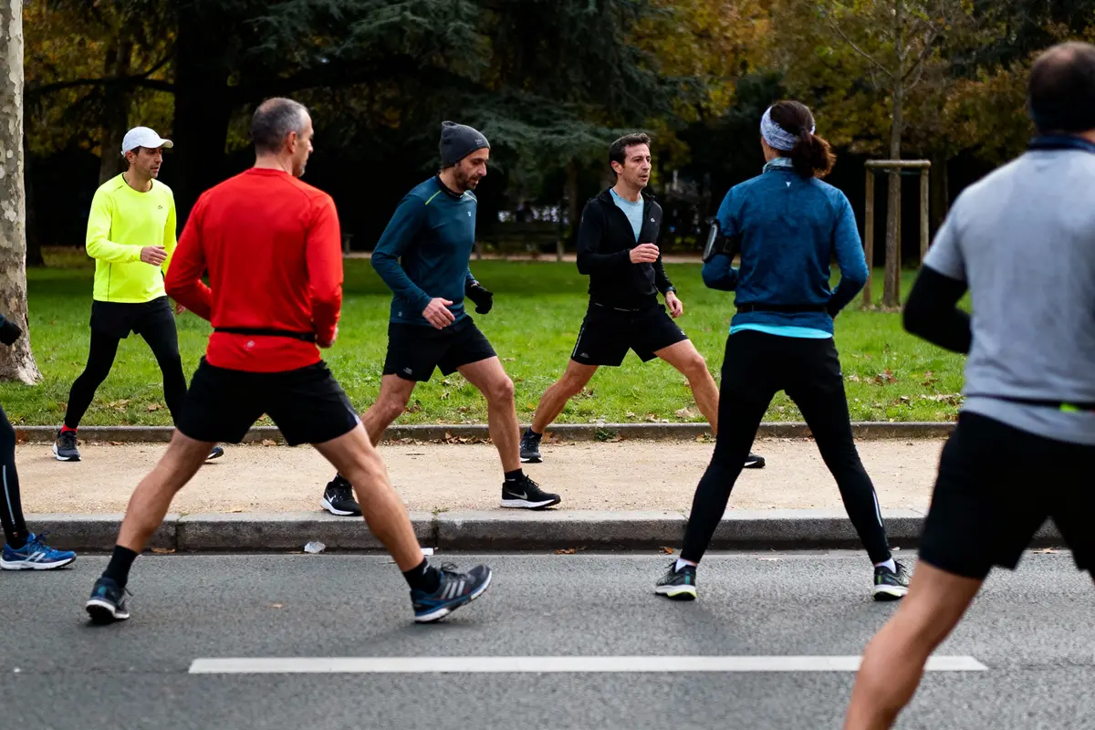 Groupe de personnes faisant des exercices de course dans un parc, entouré de verdure et d'arbres.