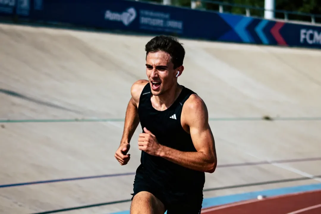 Homme courant sur une piste de course, portant un débardeur noir, affichant de la détermination.