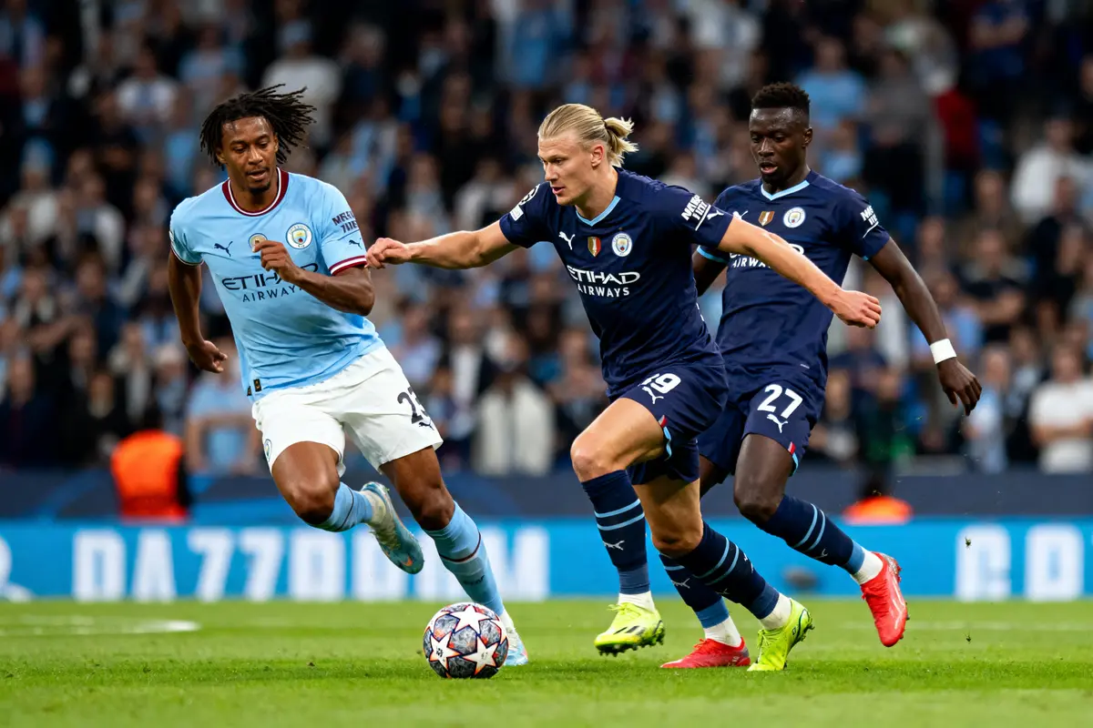 Trois joueurs de football en action sur le terrain pendant un match, portant des maillots bleus.