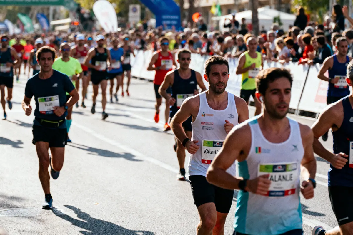 Un groupe de coureurs participe à un marathon, sur une route bordée de spectateurs et de bannières.