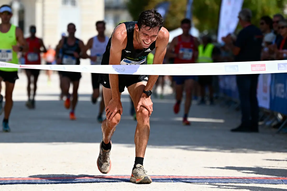 Un coureur franchissant la ligne d'arrivée d'une course, entouré par d'autres concurrents.