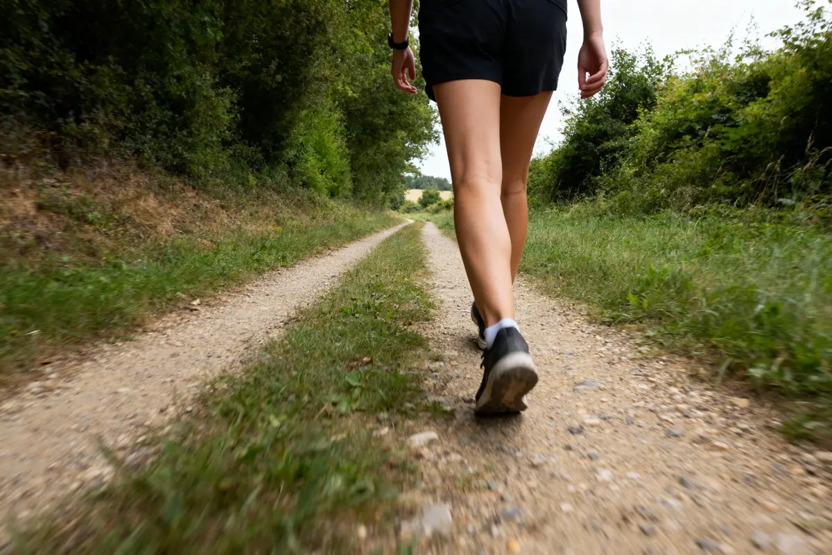 Personne marchant sur un chemin de terre entouré de végétation verte, portant shorts noirs et baskets.