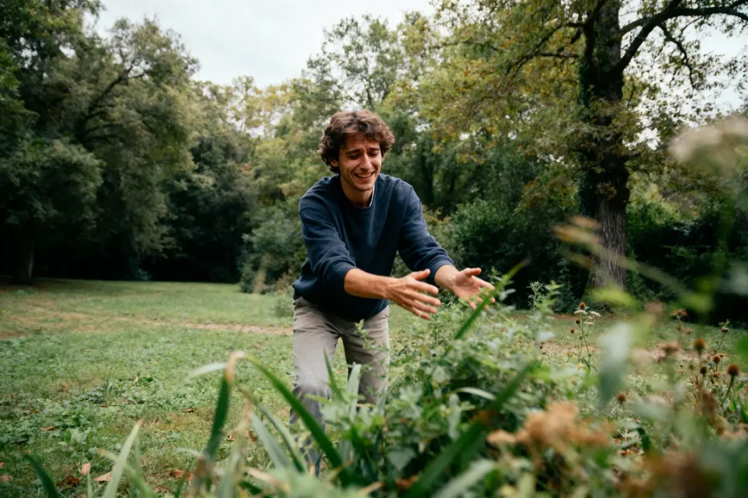 Homme souriant tend les bras dans la nature, entouré de verdure et d'arbres, en plein air.