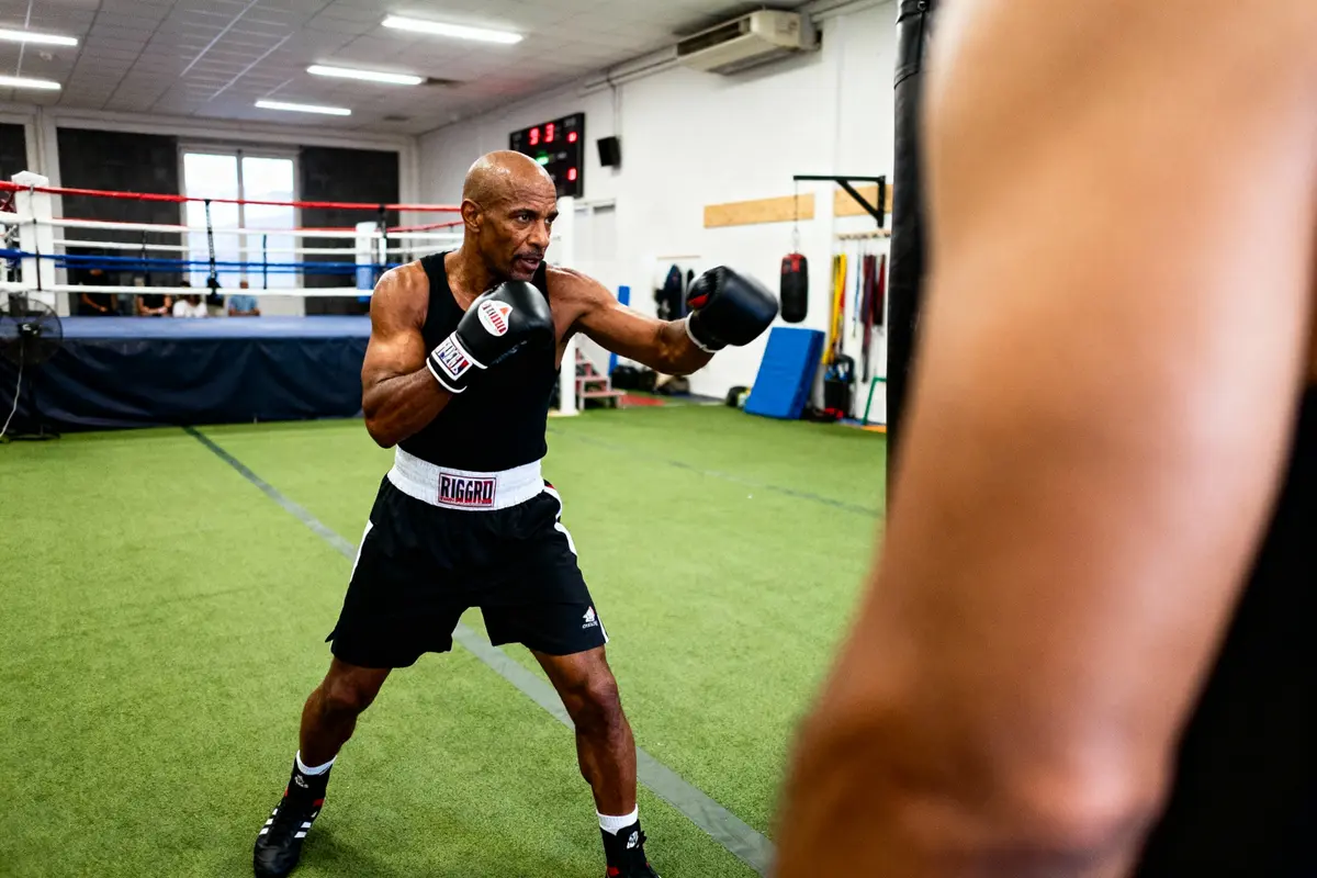 Un boxeur s'entraîne dans une salle de sport, portant des gants noirs, prêt à frapper.