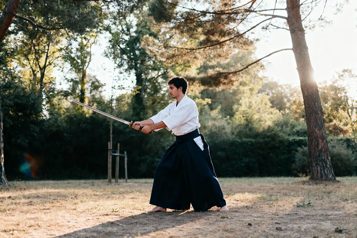 Personne pratiquant le kendo en plein air, tenue traditionnelle, forêt en arrière-plan, lumière douce du soir.