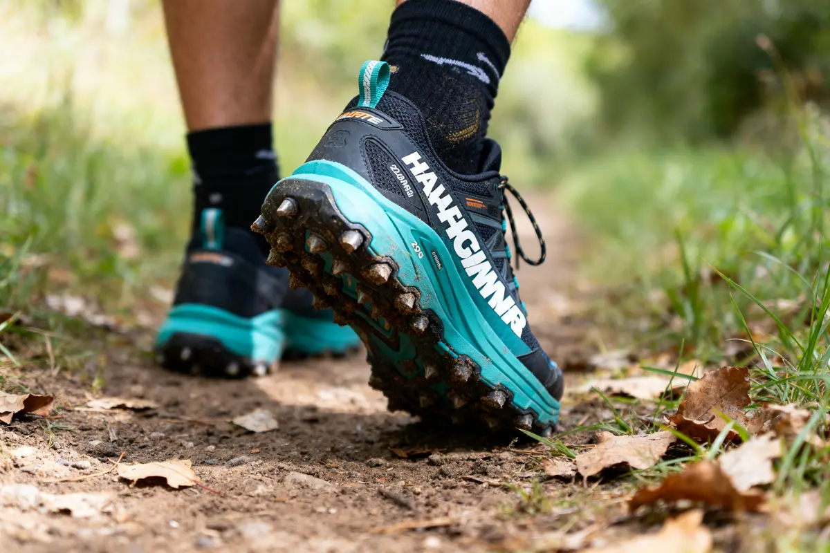 Gros plan sur des chaussures de trail sur un chemin forestier avec feuilles mortes et herbe.