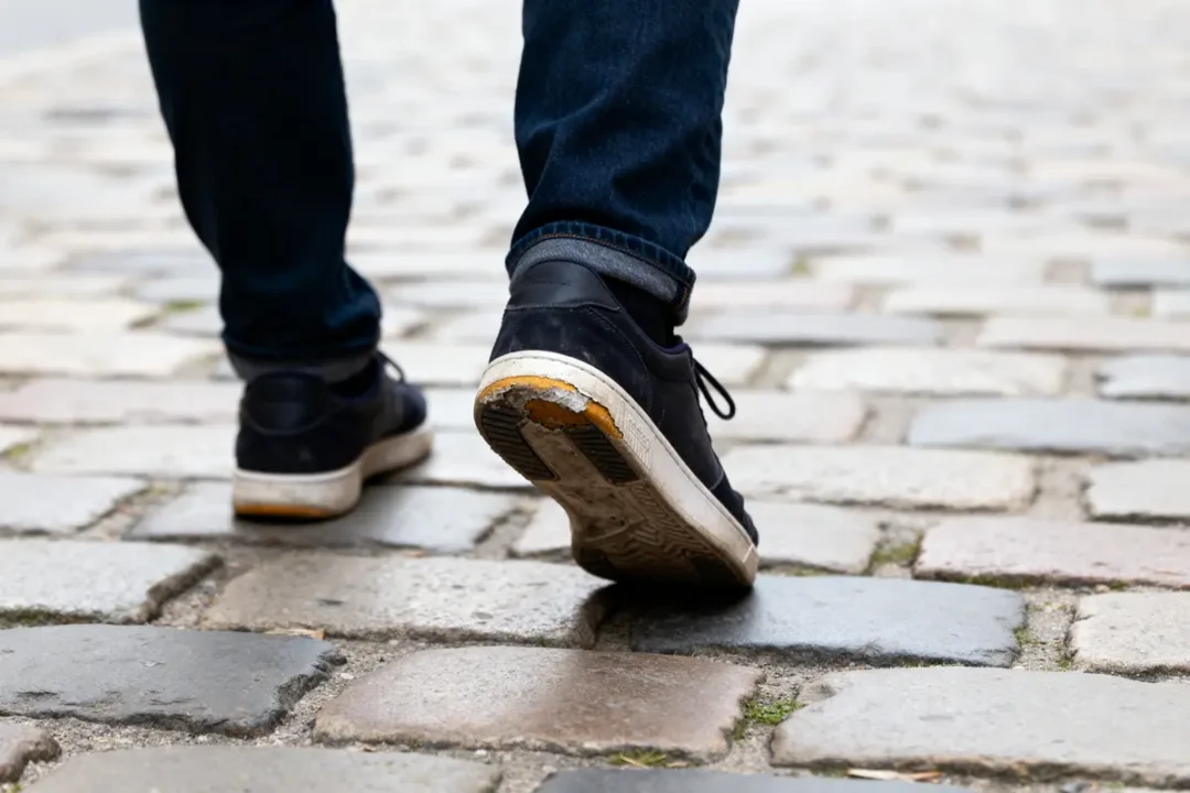 Personne marchant sur des pavés avec des chaussures usées, illustrant la façon de supinierer