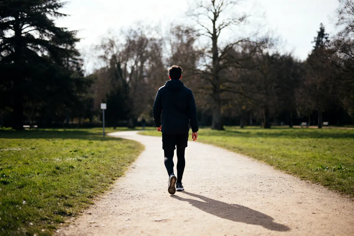 Un homme marche sur un chemin de parc, illustrant 20000 pas en km quotidiennement