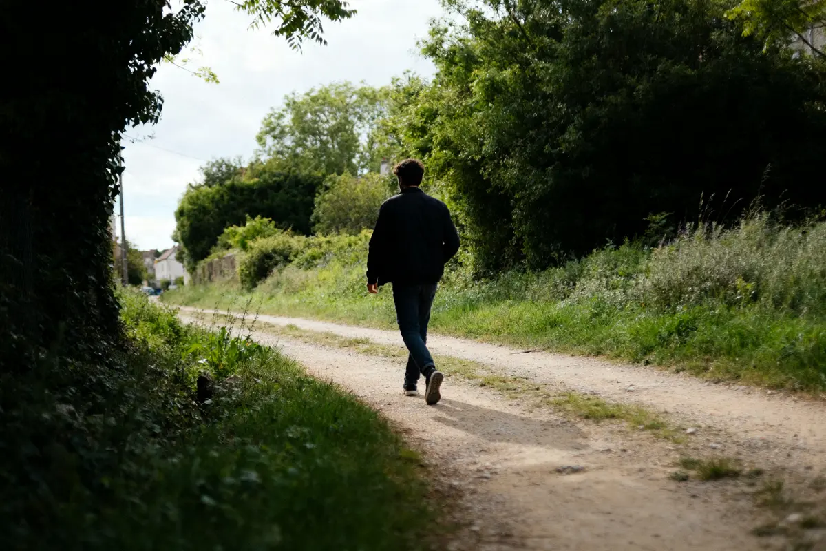Un homme marche seul sur un chemin rural symbolisant 20000 pas en km parcourus.