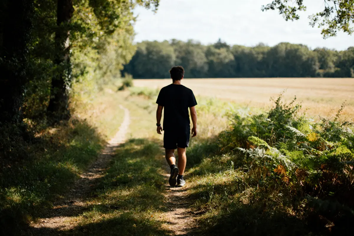 Homme marchant sur un sentier forestier, illustrant 20000 pas en km dans la nature