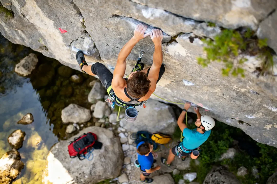 Un grimpeur escalade une falaise rocheuse, observé par des partenaires, scène typique de planet grimpe