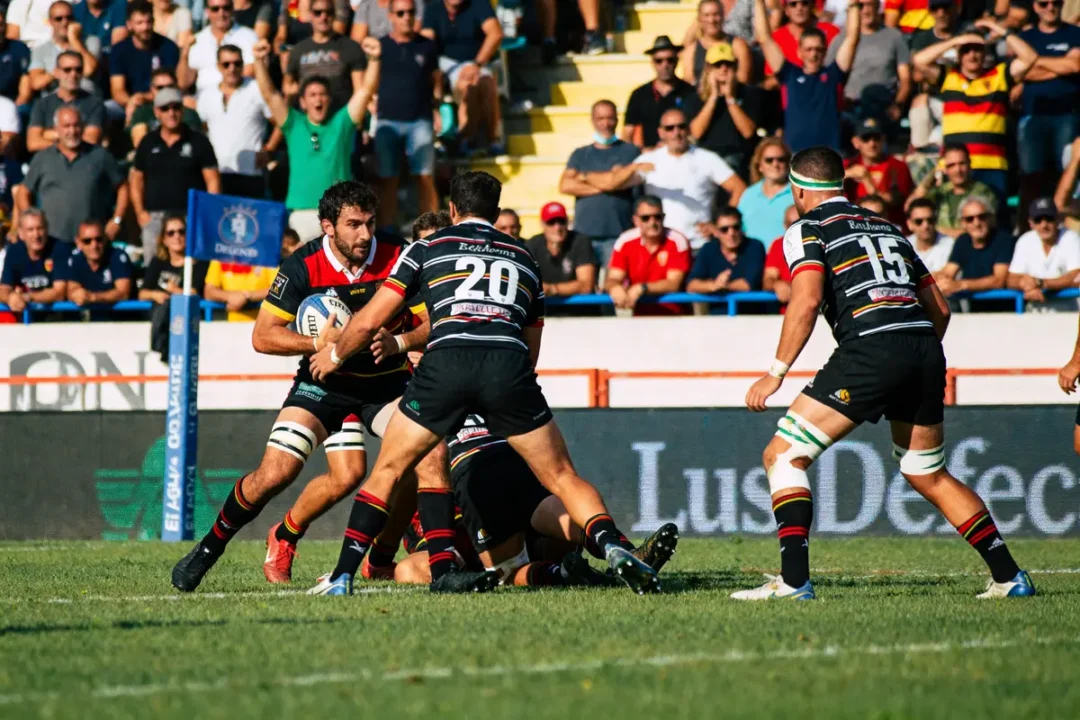Rugby à céret sportif, joueur avec ballon attaqué par trois adversaires devant public enthousiaste