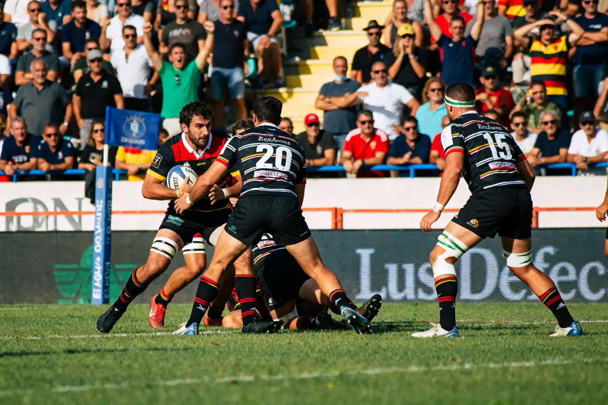 Rugby à céret sportif, joueur avec ballon attaqué par trois adversaires devant public enthousiaste