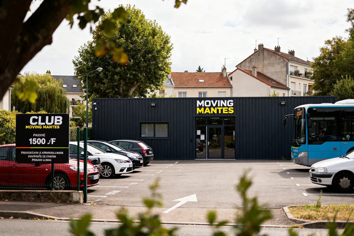 Bâtiment du club Moving Mantes avec parking et bus devant des maisons résidentielles