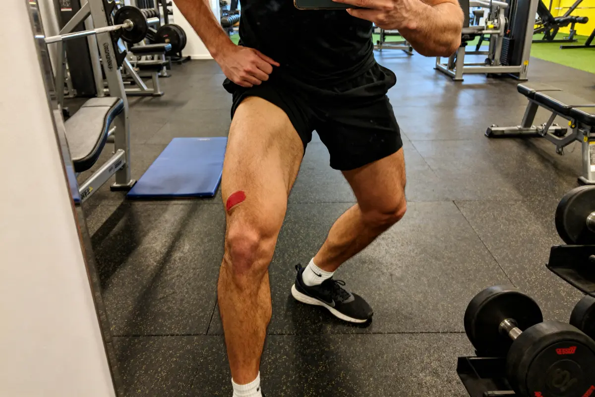 Homme au gymnase montrant sa jambe musclée après extension de quadriceps avec bande kinésio rouge