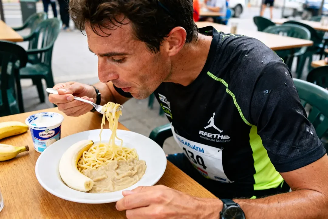 Homme mangeant des pâtes et une banane, préparation énergétique pour marathon alimentation.