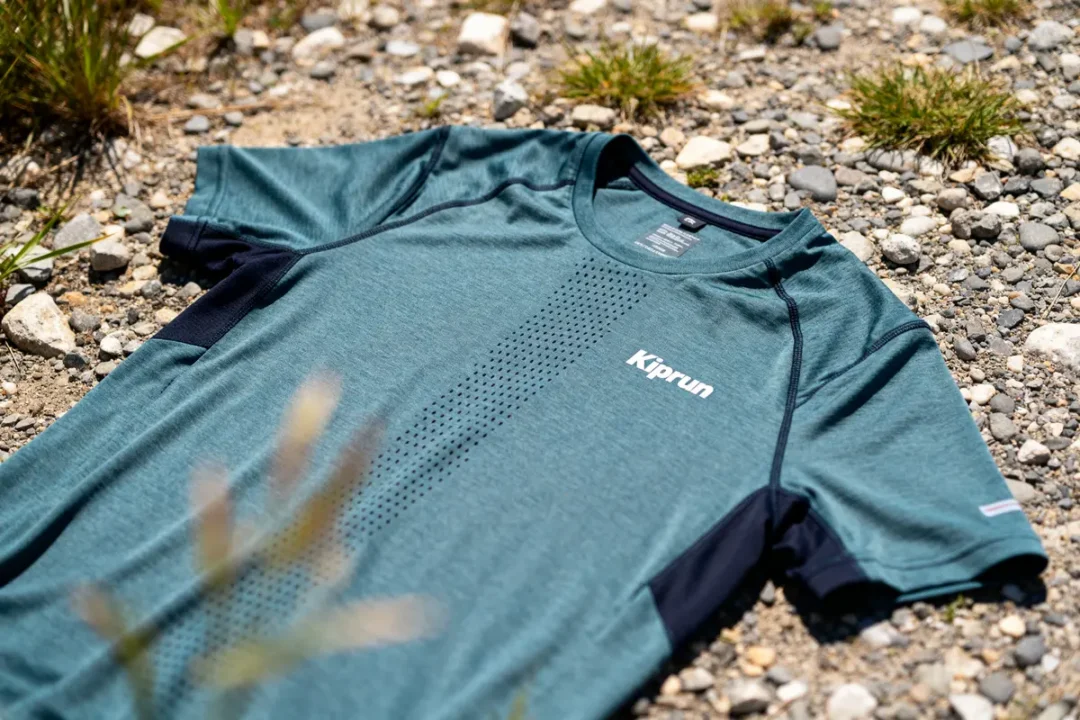 T-shirt Kiprun bleu posé sur sol caillouteux avec herbes sèches autour