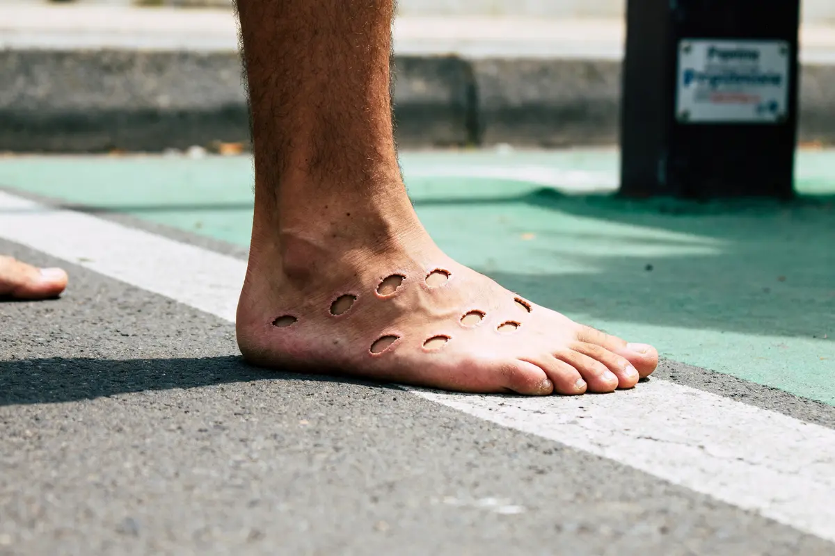 Pied avec motifs circulaires évoquant la trypophobie, posé sur une route.